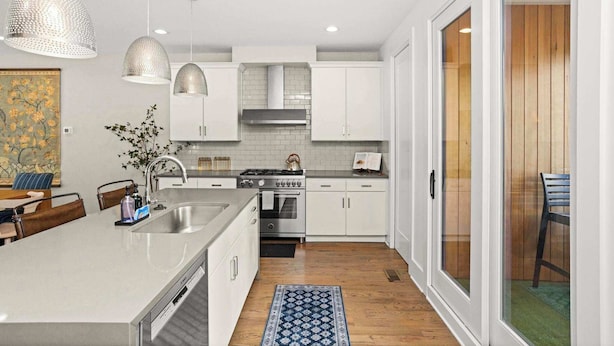 A modern kitchen with white cabinets, a central island, pendant lighting, and a view to a wooden deck. - 2 Homes-Sleeps 24 | Downtown Great for Big Groups! (Nashville)