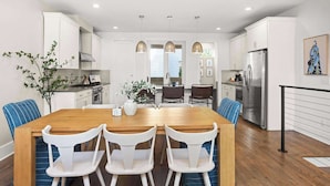 A modern kitchen with white cabinets, a wooden dining table, and blue chairs. - 2 Homes-Sleeps 24 | Downtown Great for Big Groups! (Nashville)
