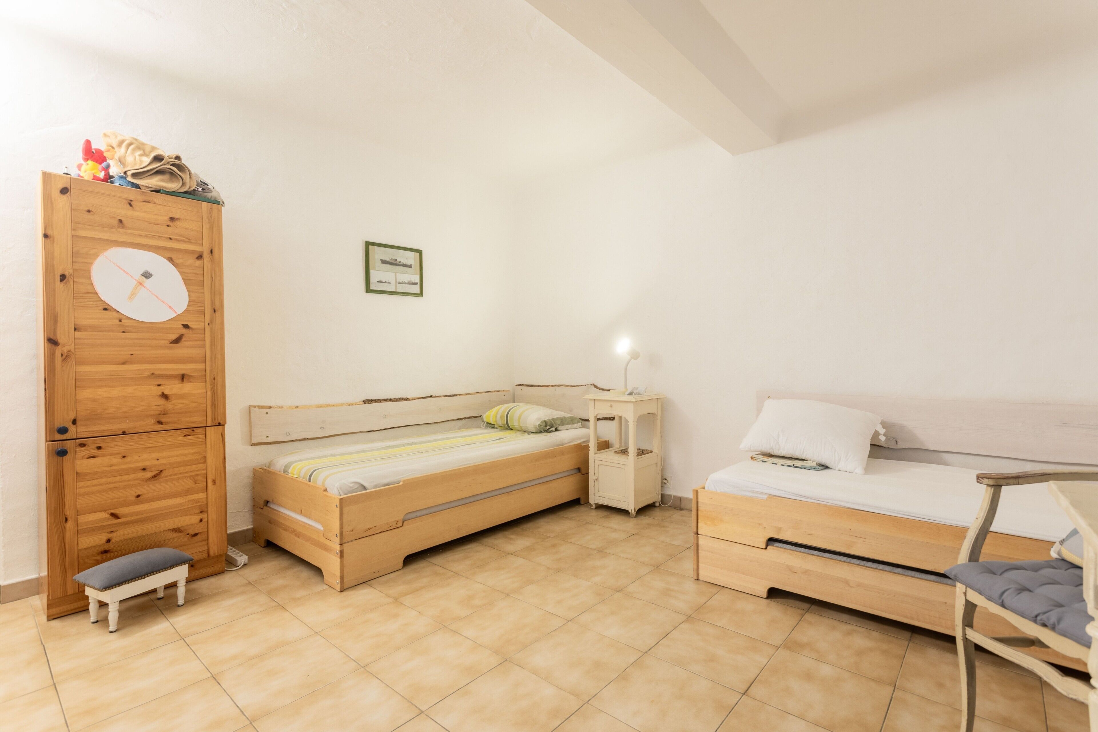 Une chambre à coucher avec deux lits en bois, un petit banc, une table de chevet et une armoire en bois.