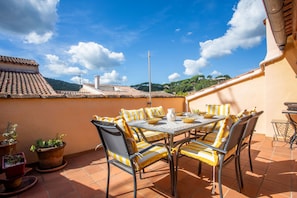 Una terraza con una mesa y sillas, plantas en macetas y vistas de los edificios y colinas circundantes.