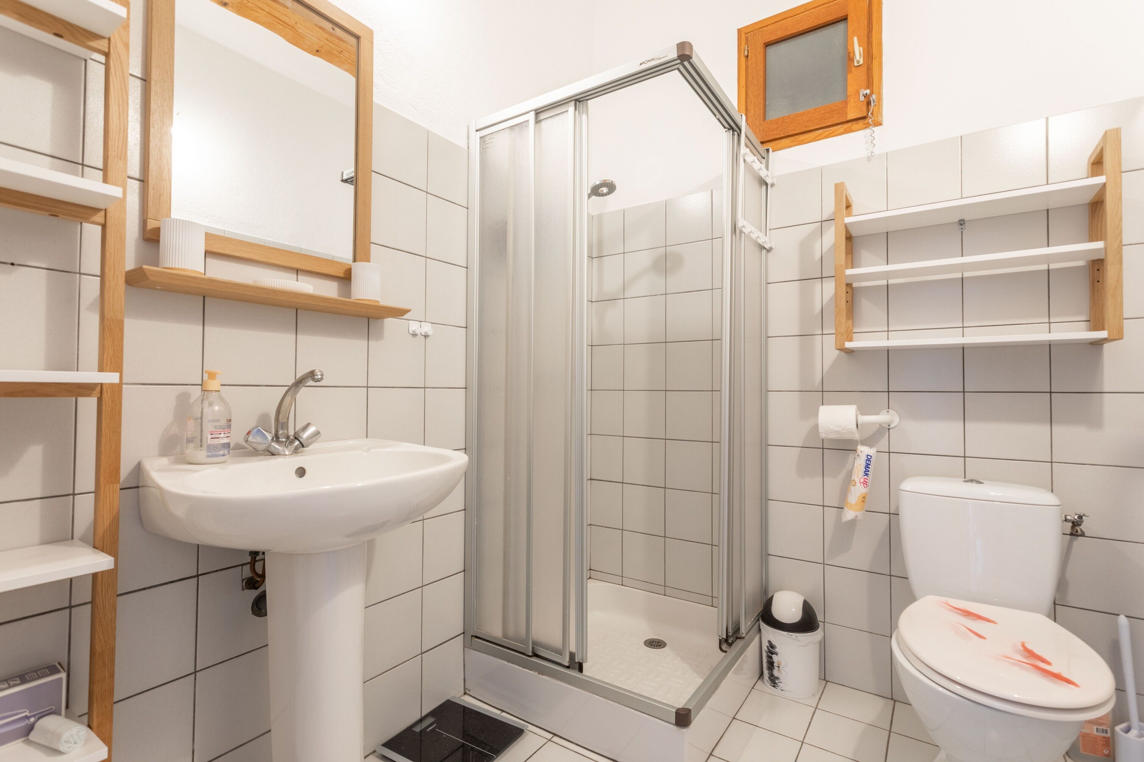 A bathroom with a shower, sink, toilet, and shelves.