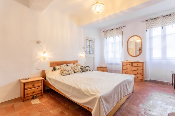 Un dormitorio con cama, mesitas de noche, cómoda, espejo y lámpara de araña.