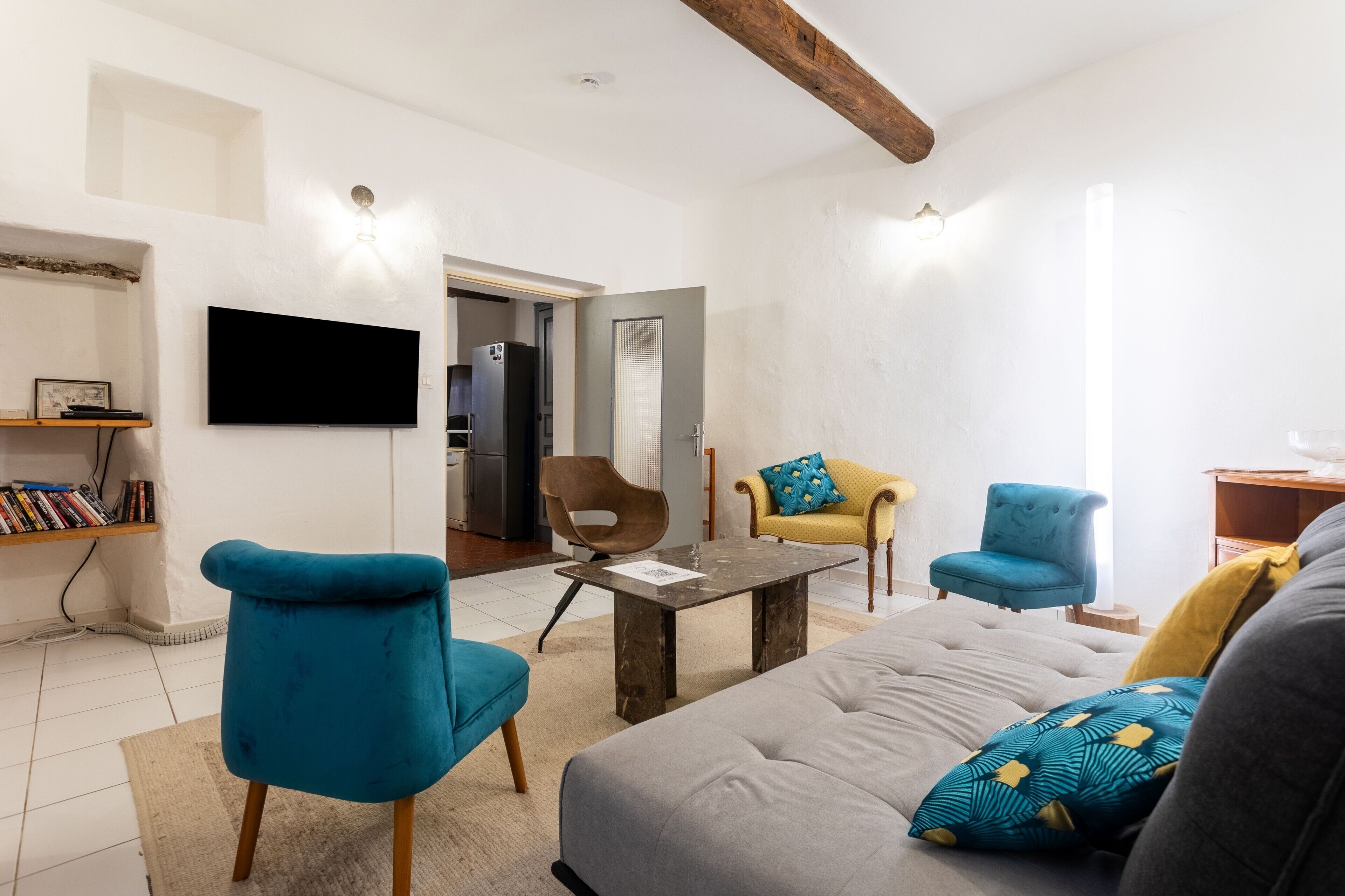 A modern living room with a sofa, two armchairs, a coffee table, a flat-screen TV, and a bookshelf.