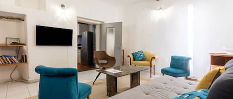 A modern living room with a sofa, two armchairs, a coffee table, a flat-screen TV, and a bookshelf.