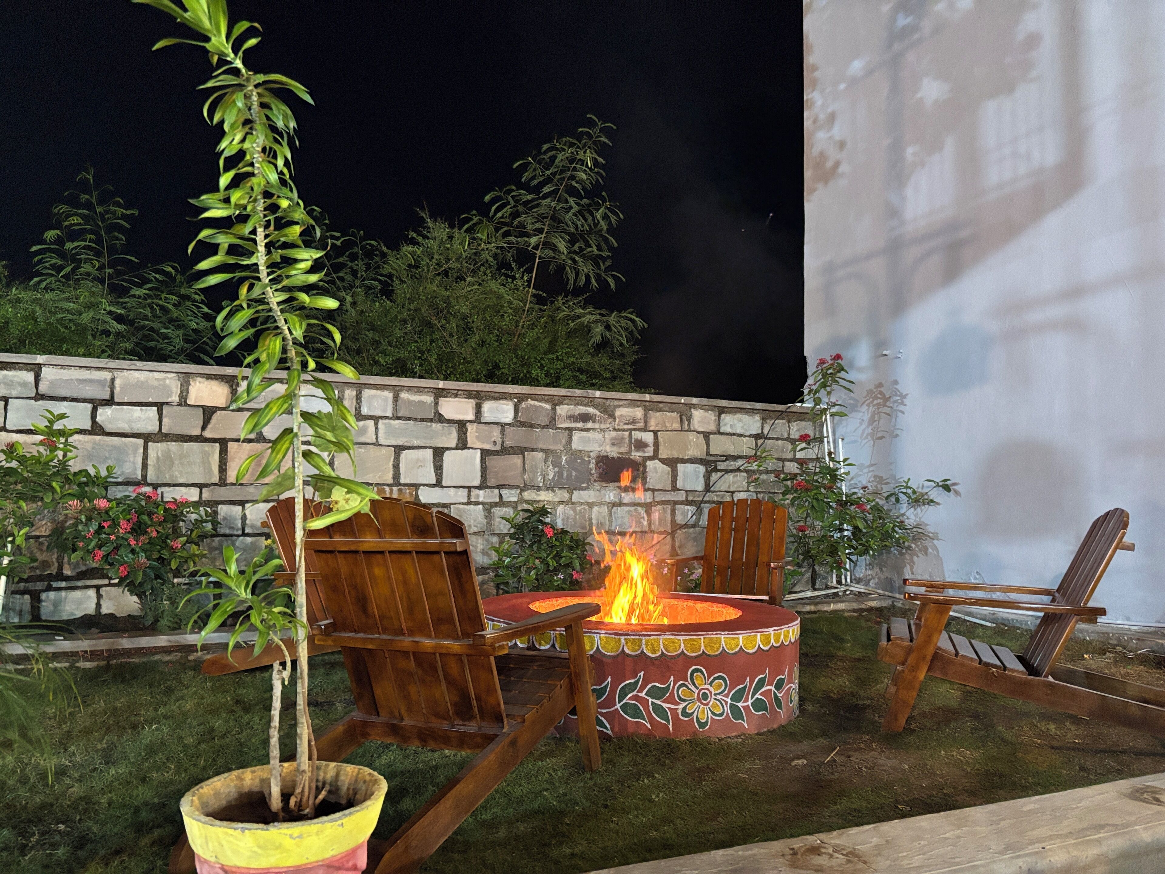 An outdoor seating area with a fire pit, wooden chairs, and a potted plant.