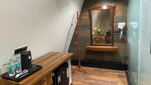 Ein Hotelzimmer mit einem Holztisch, einem Spiegel, einer Stehlampe und einer Duschkabine aus Glas.
