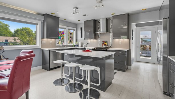 A modern kitchen with a central island, bar stools, stainless steel appliances, and a view of the outdoors. - Top-level duplex featuring a sleek open concept kitchen with stainless appliances, cozy fireplace, stylish furnishings, and in-unit washer/dryer. Designed for basking in the sun under skylights in thoughtful details throughout. (Vancouver)