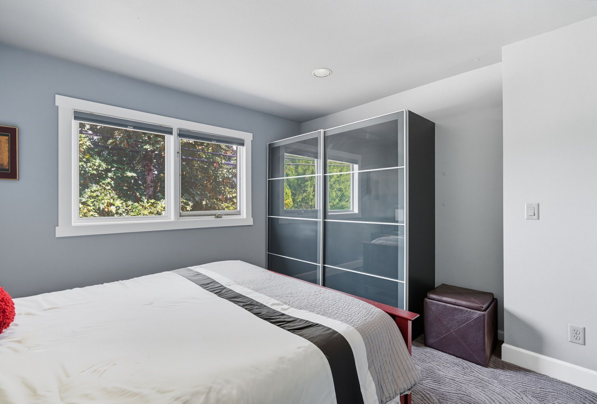 A bedroom with a bed, a wardrobe, and a window with a view of trees.