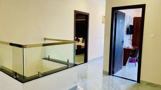 Un passadís amb barana de vidre, una porta que dona a una habitació amb llit i un escriptori amb cadira.