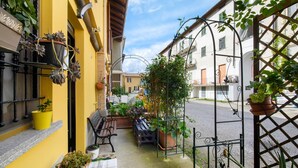 Una calle estrecha con balcones, plantas en macetas y mesas al aire libre.