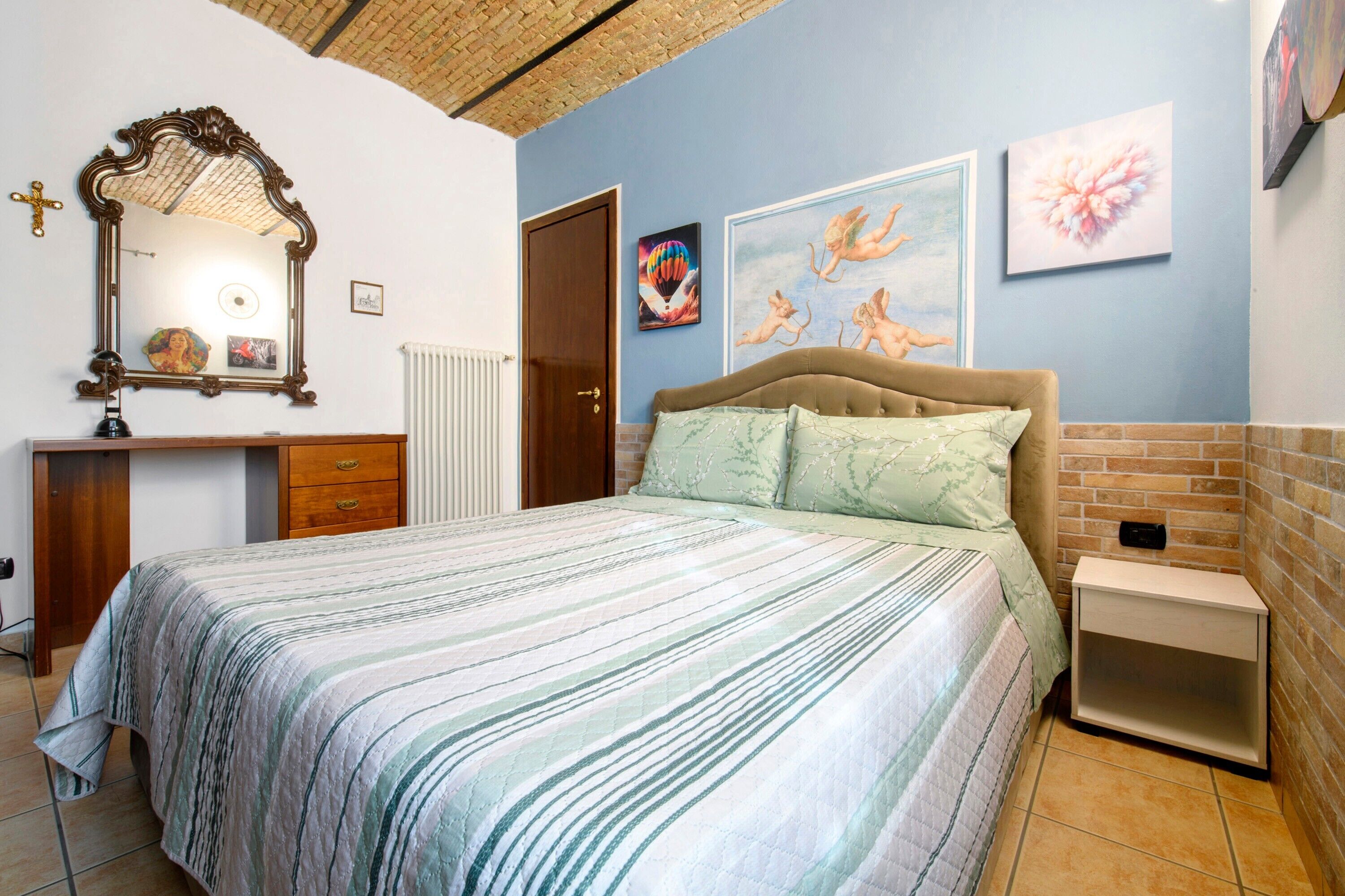 Ein Schlafzimmer mit Bett, Nachttisch, Kommode, Spiegel und Bildern an den Wänden.