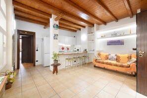 A spacious living area with a wooden ceiling, a sofa, a dining table with chairs, and a kitchen in the background.