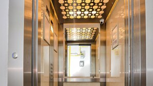 En elevator med metallisk indretning, et mønstret loft og et lille kontrolpanel.