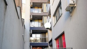 En smal trappe fører op til en bygning med flere etager, altaner, ventilationsanlæg og en rød dør.
