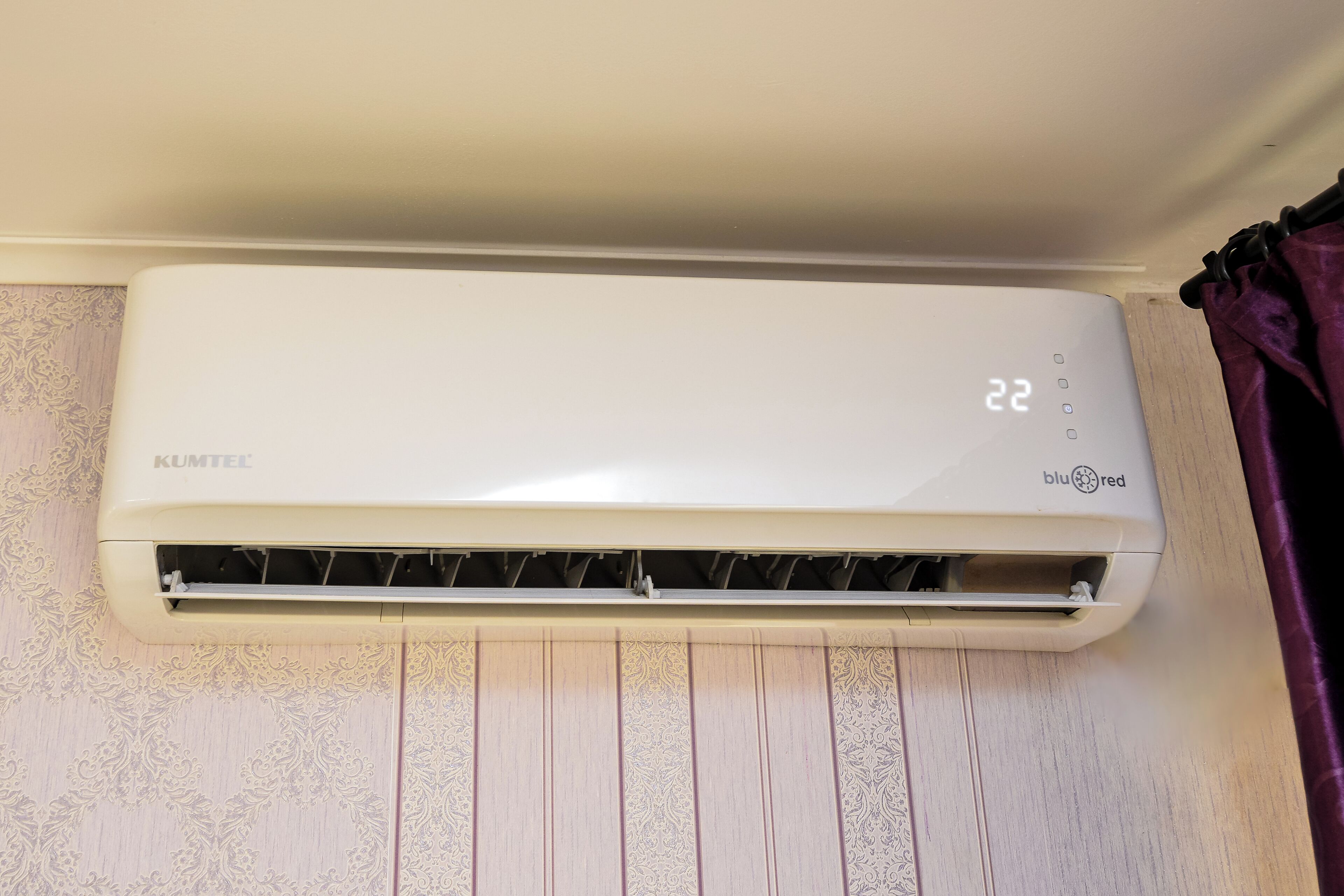 A white air conditioning unit mounted on a wall with a patterned wallpaper design below.