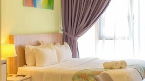 A hotel room with a bed, a nightstand, a lamp, a painting on the wall, and a window with curtains. - Flypod Hotel (Kota Kinabalu)