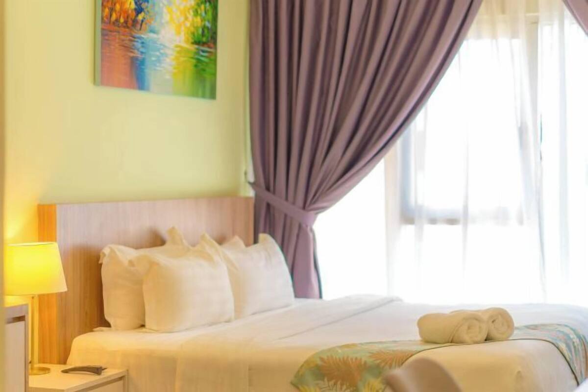 A hotel room with a bed, a nightstand, a lamp, a painting on the wall, and a window with curtains.