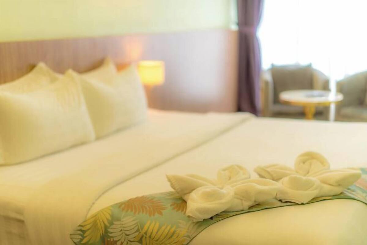 A hotel room with a bed, pillows, a bedside lamp, a chair, and a small round table.