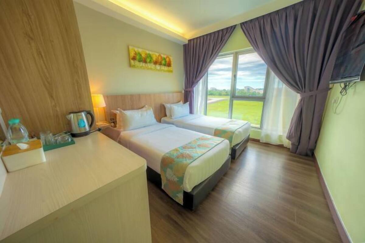 A hotel room with two beds, a wooden desk, a painting on the wall, and a view of a green landscape through the window.