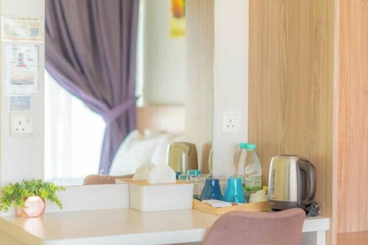 A hotel room with a desk, a mirror, a potted plant, a kettle, and a water bottle.