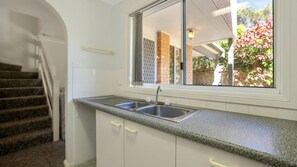 Une cuisine dotée d’un évier à deux bacs, de meubles blancs et d’une fenêtre donnant sur un jardin.