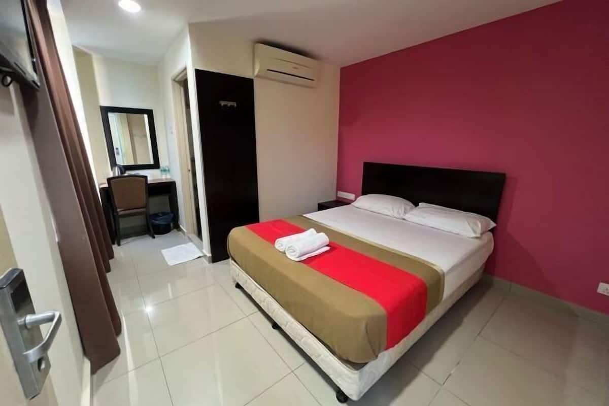Una camera d'albergo con un letto, una scrivania, una sedia, uno specchio e un condizionatore d'aria.