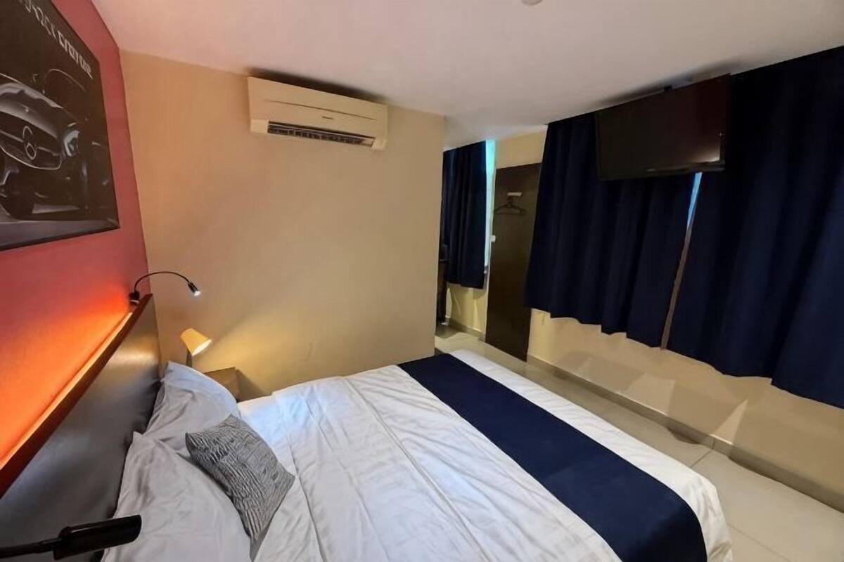 Ein Hotelzimmer mit einem Bett, einem Nachttisch, einer Wandklimaanlage, einem Spiegel und einem Fenster mit Vorhängen.