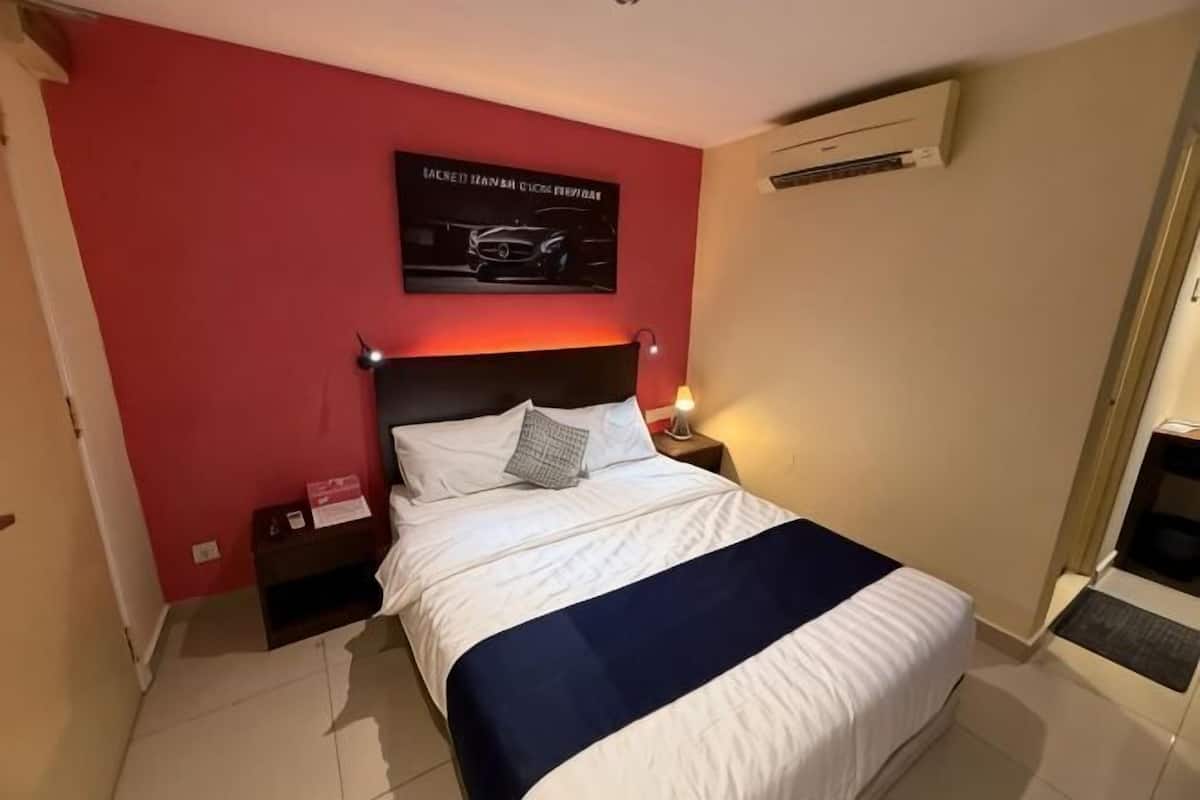 Una camera d'albergo con un letto, comodini, un condizionatore d'aria a muro e una porta.