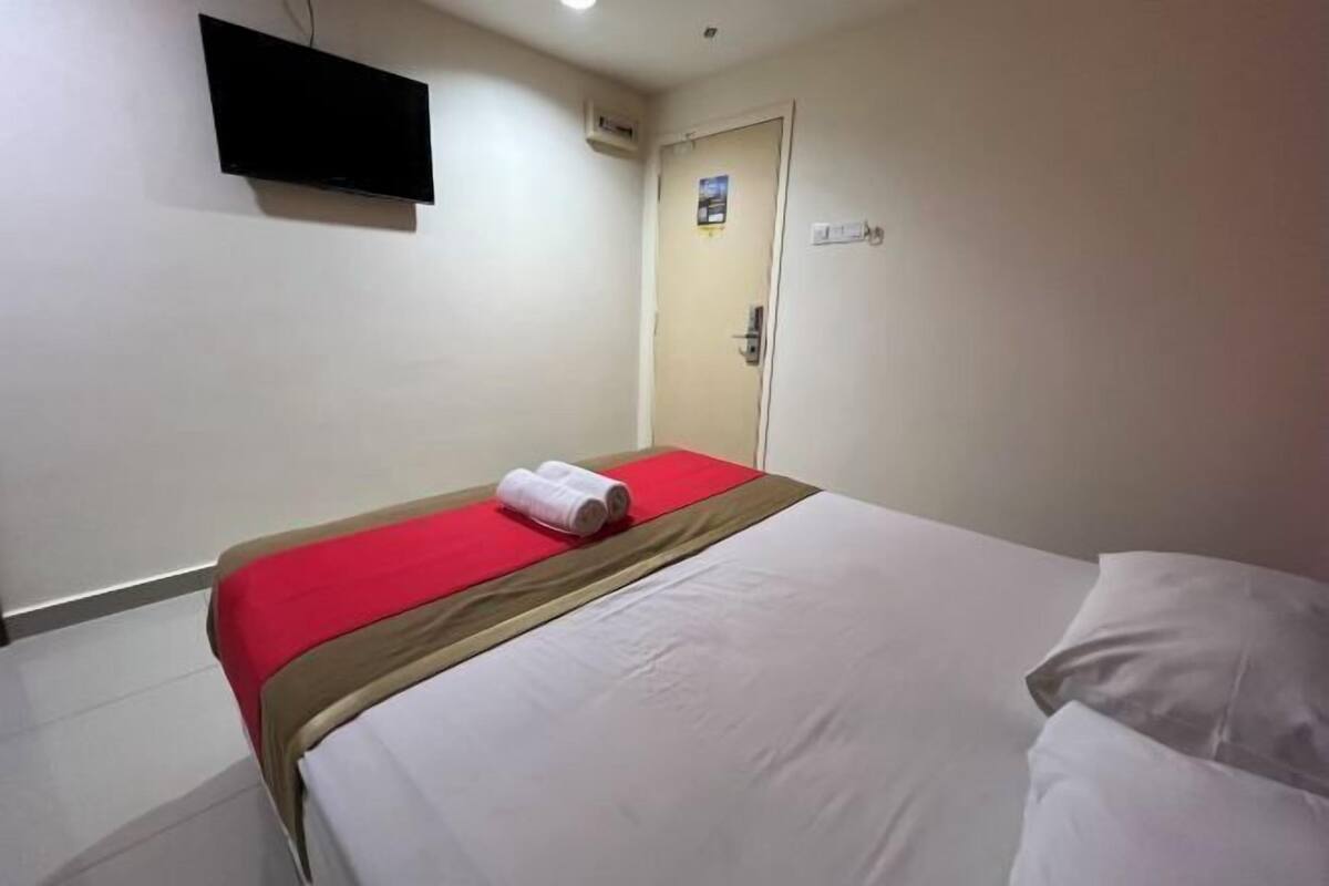 Una camera d'albergo con un letto, una TV a schermo piatto fissata al muro, una porta e un piccolo quadro appeso alla porta.