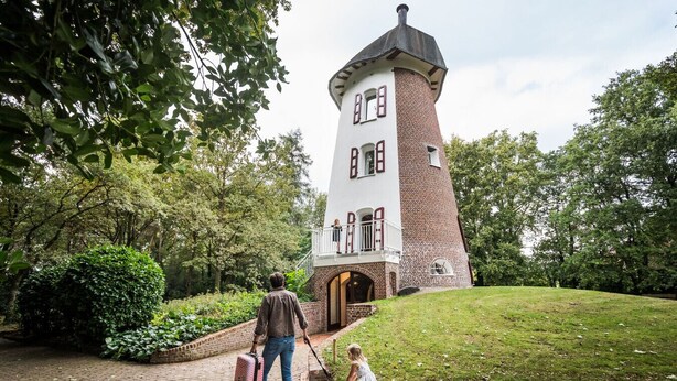 Ein Backsteinturm mit Balkon, umgeben von viel Grün.