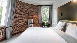 Ein Schlafzimmer mit Ziegelwand, einem großen Bett, einem Fenster mit Vorhängen und einer Pflanze.