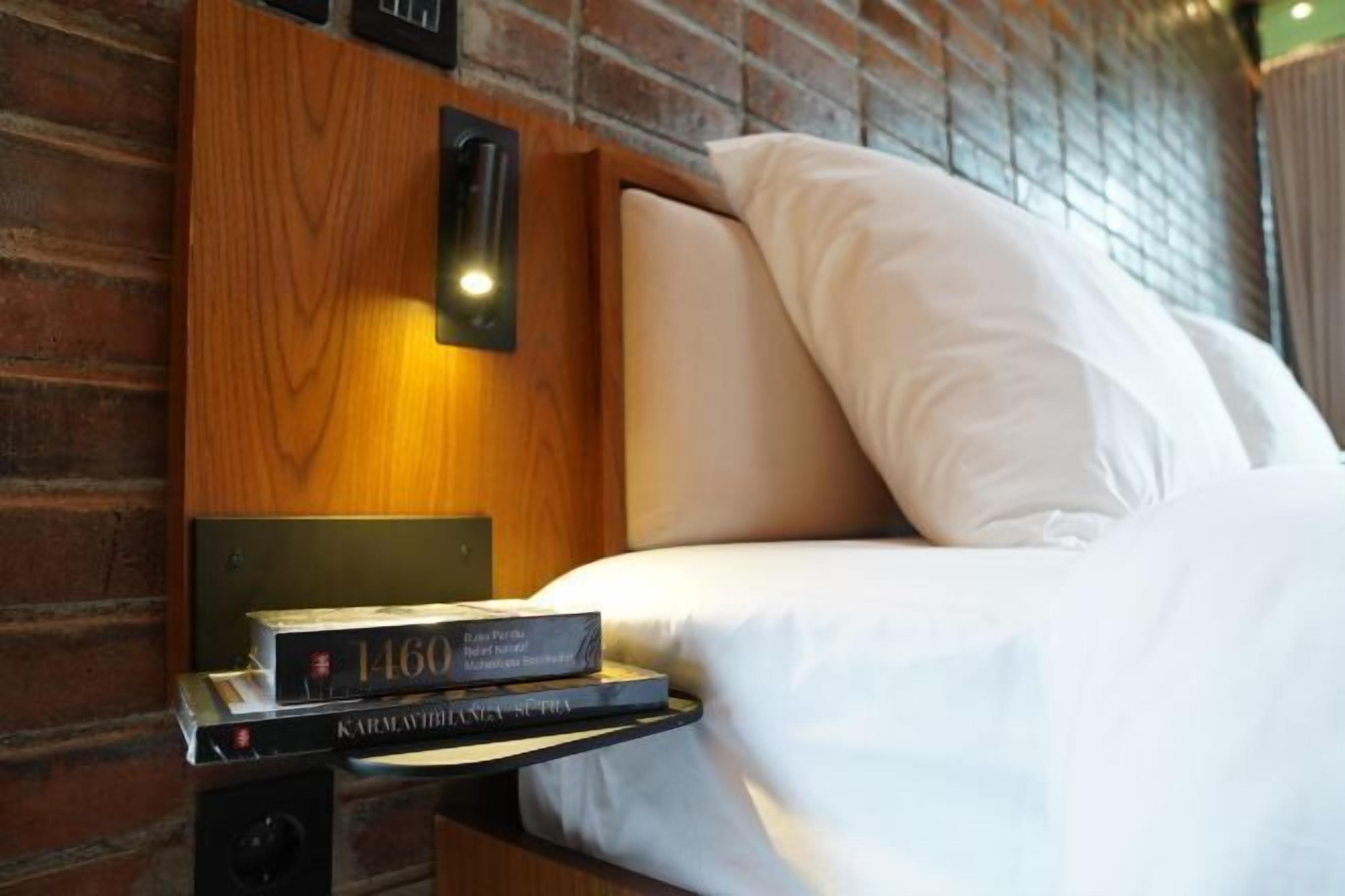 A neatly made bed with white linens, a bedside lamp, and a book titled "1460" on a wooden nightstand.