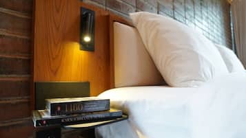 A neatly made bed with white linens, a bedside lamp, and a book titled "1460" on a wooden nightstand.