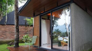 A modern house with a wooden deck, a green chair, and a glass door leading to a patio area. - Tanawana Living Borobudur (Borobudur)