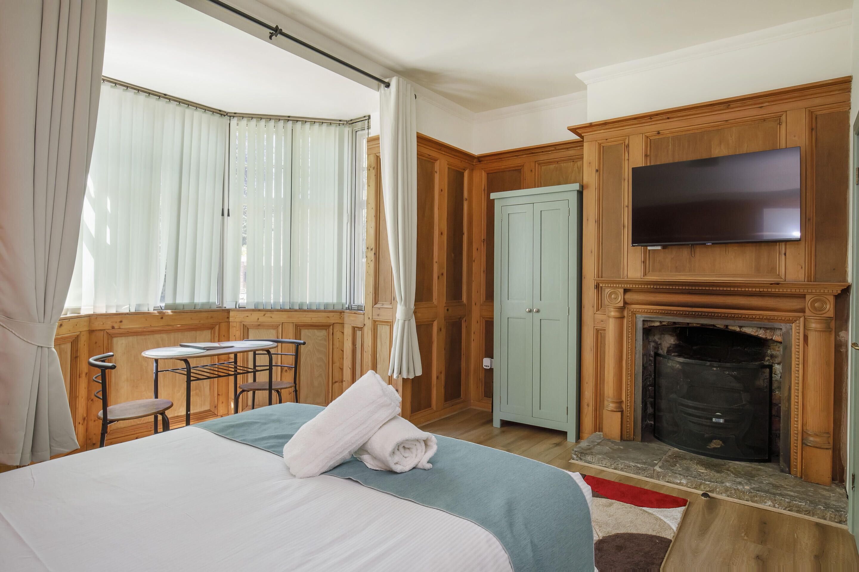 Een slaapkamer met een bed, een televisie, een open haard en een raam met gordijnen.