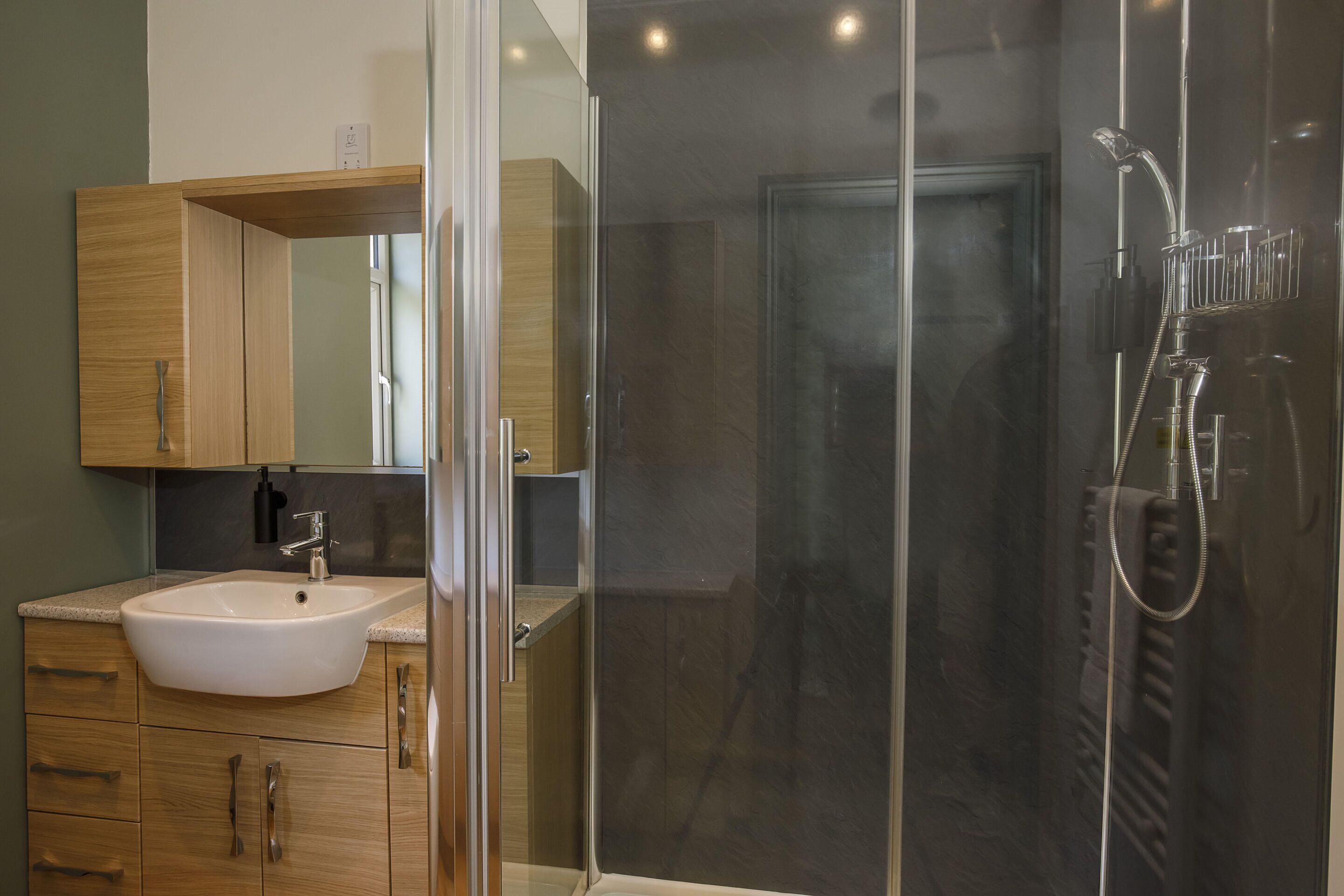 A modern bathroom with a glass shower enclosure, a sink, and wooden cabinets.