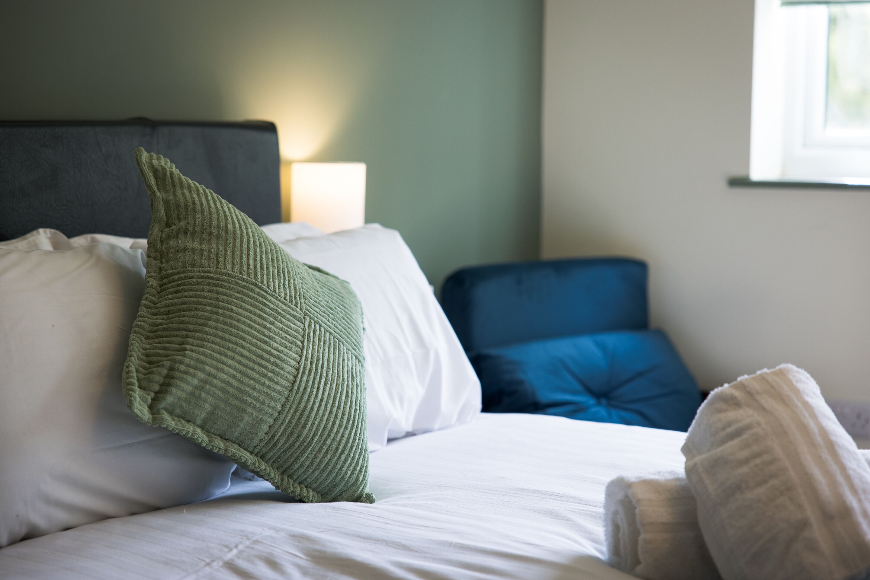 A bed with white bedding and a green knitted throw pillow.