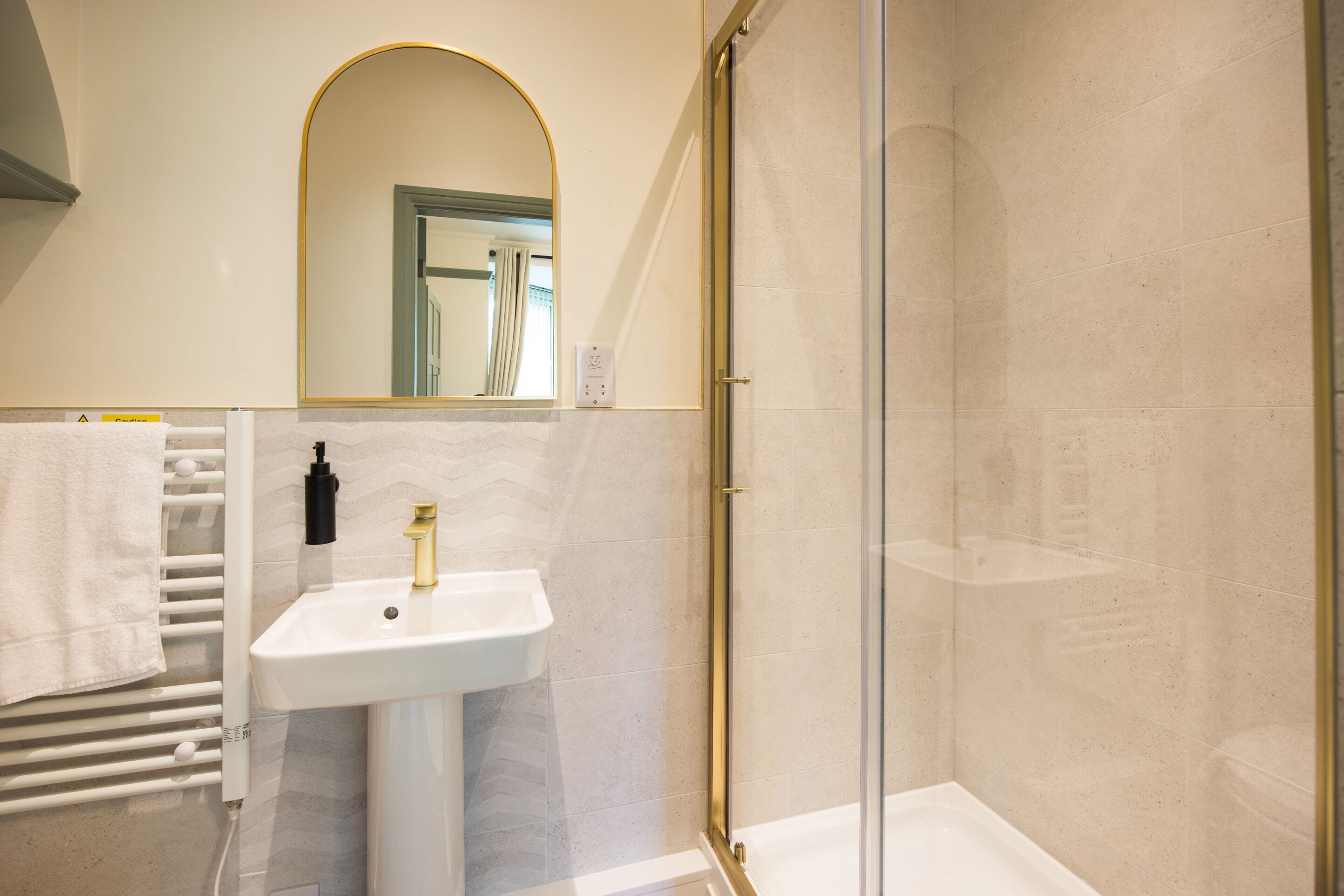 Ein Badezimmer mit einem weißen Waschbecken, einem Spiegel und einer Duschkabine aus Glas.