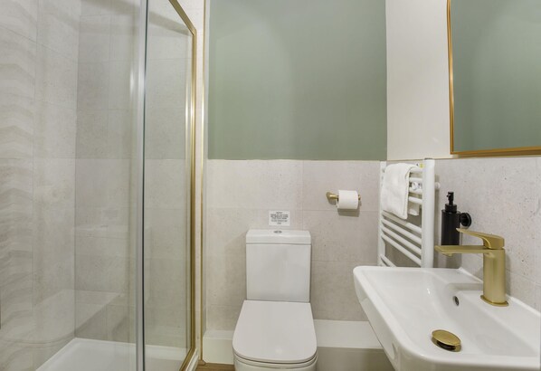 A bathroom with a glass shower enclosure, a toilet, a sink with a gold faucet, and a towel rack.
