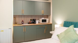 Una habitación compacta con kitchenette, una cama con almohada verde y una mesita de noche.