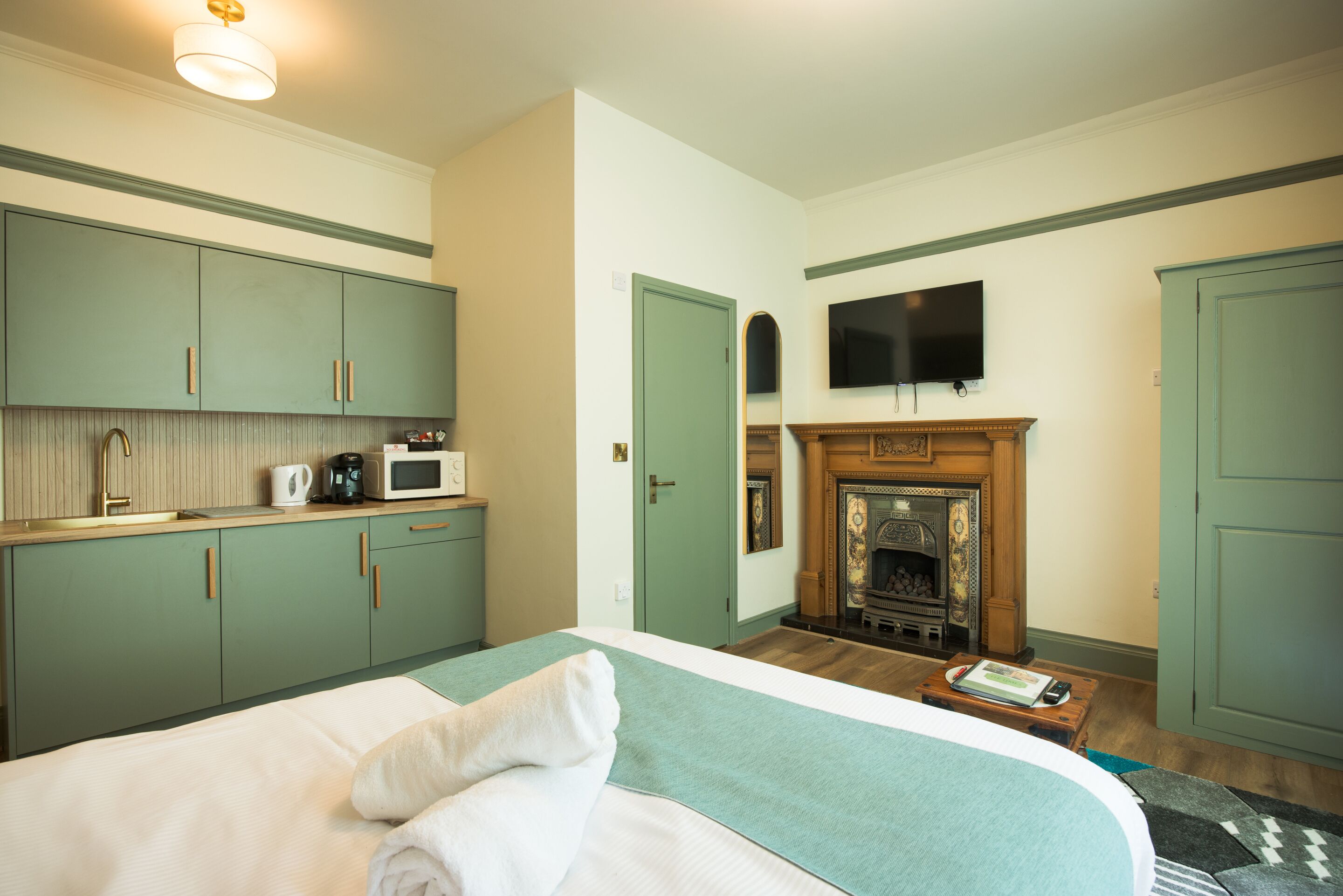 Une chambre dotée d’un lit, d’un téléviseur à écran plat fixé au-dessus d’une cheminée, et d’une kitchenette équipée d’un four à micro-ondes et d’une bouilloire.