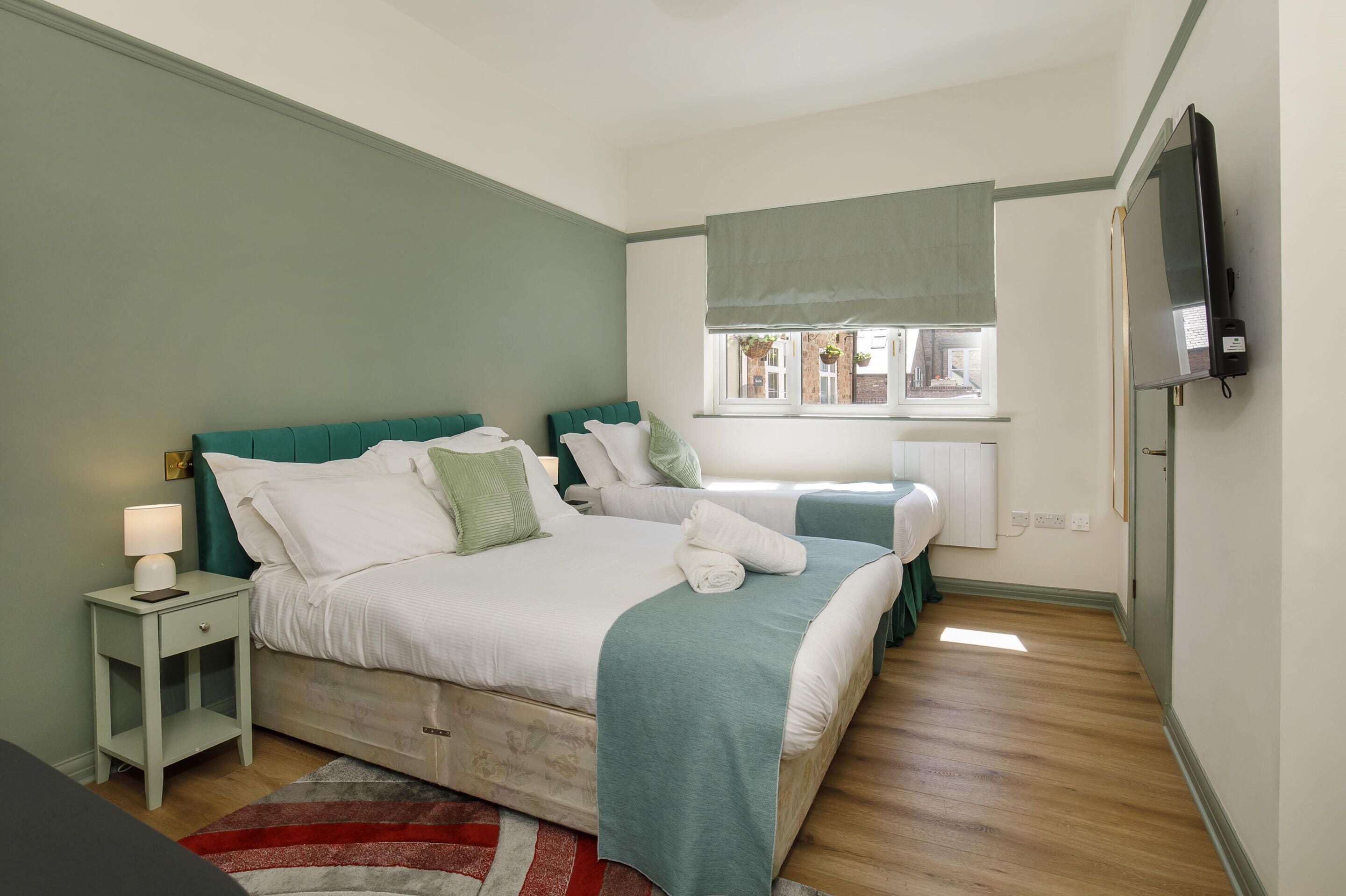A bedroom with two beds, a nightstand, a TV, and a window with a view.