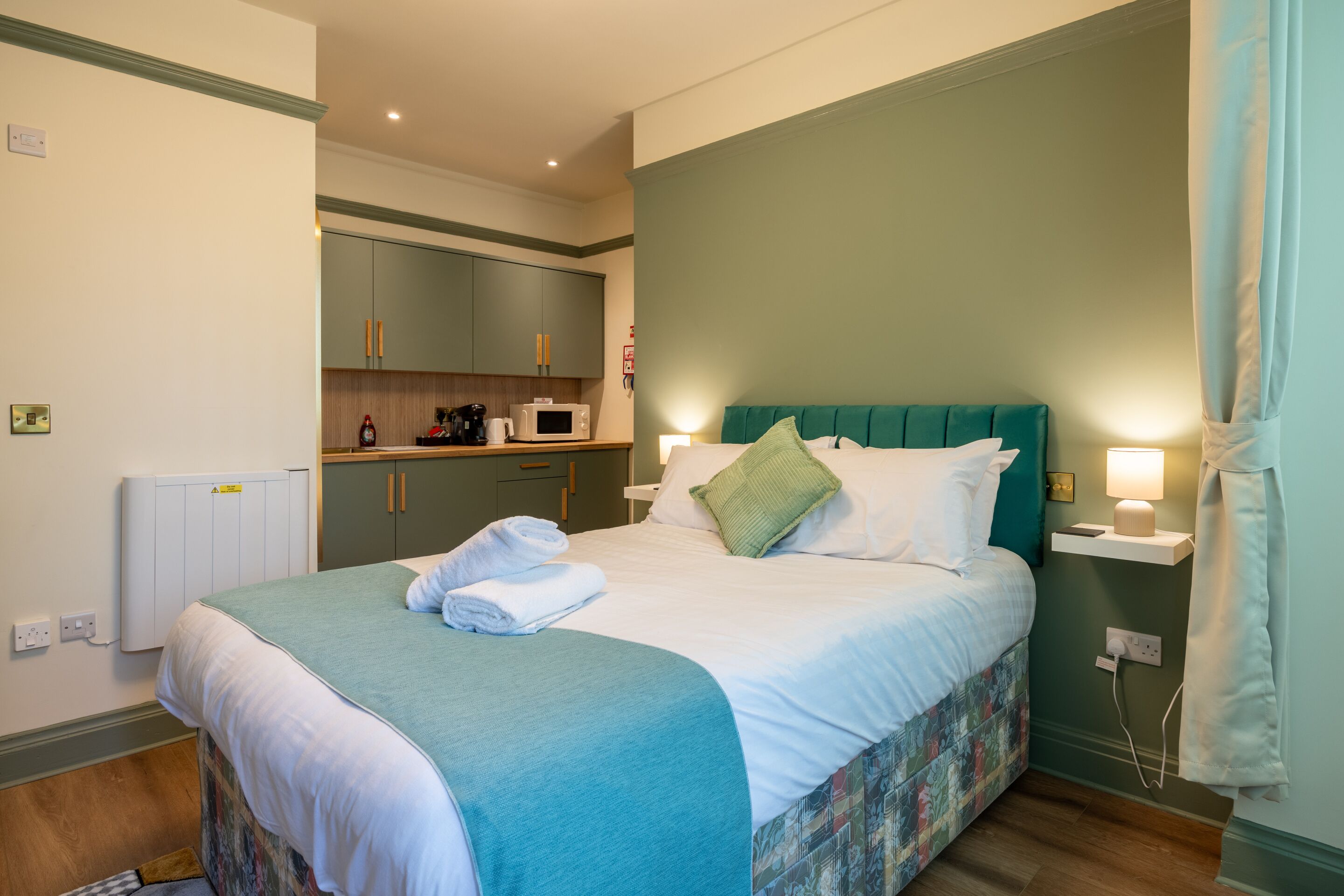 A hotel room with a bed, a small kitchenette, and a bathroom.