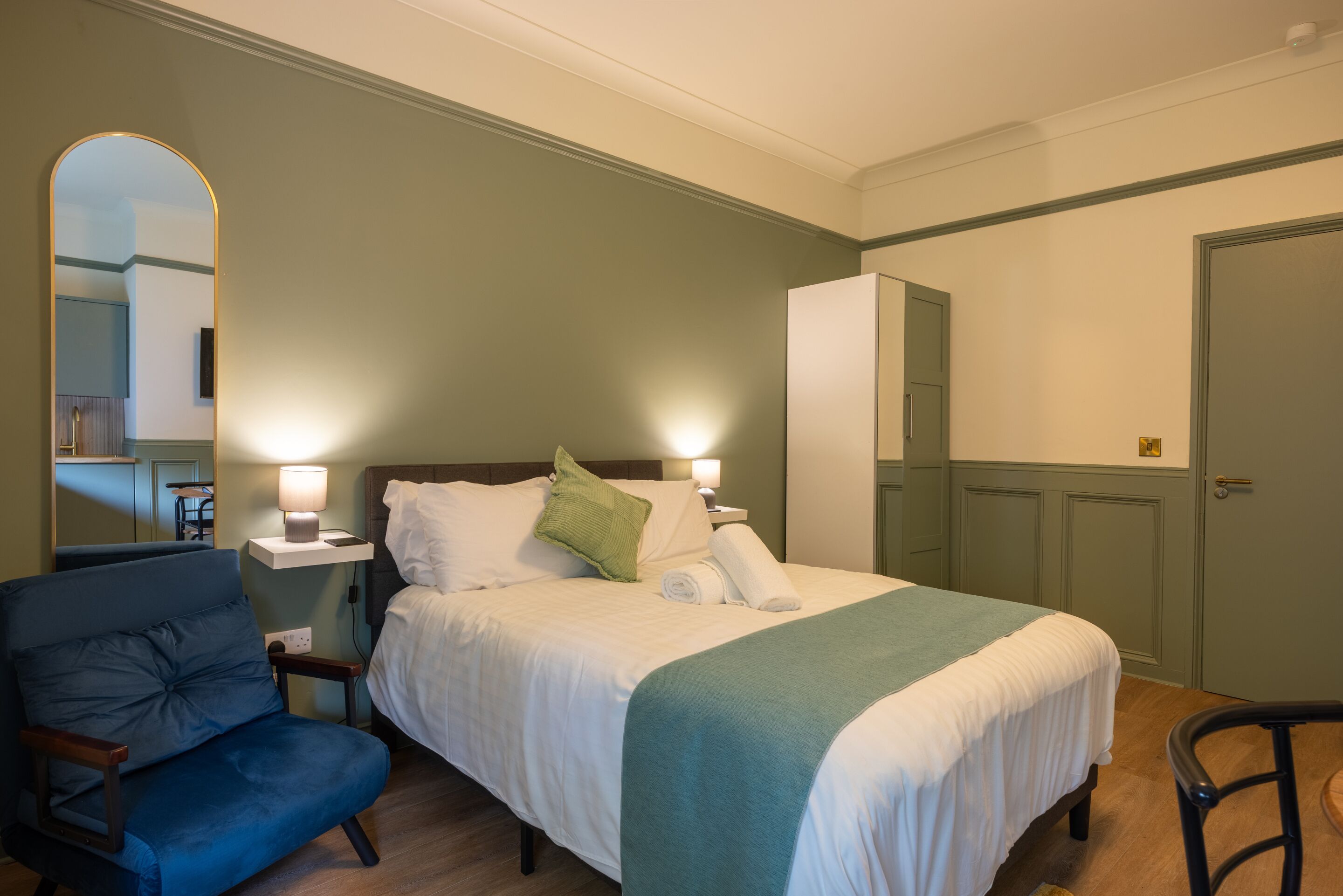 Hotellihuone, jossa on sänky, tuoli, työpöytä ja vaatekaappi.