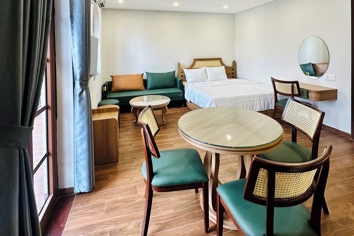 A hotel room with a bed, a sofa, a dining table with chairs, and a small round table.