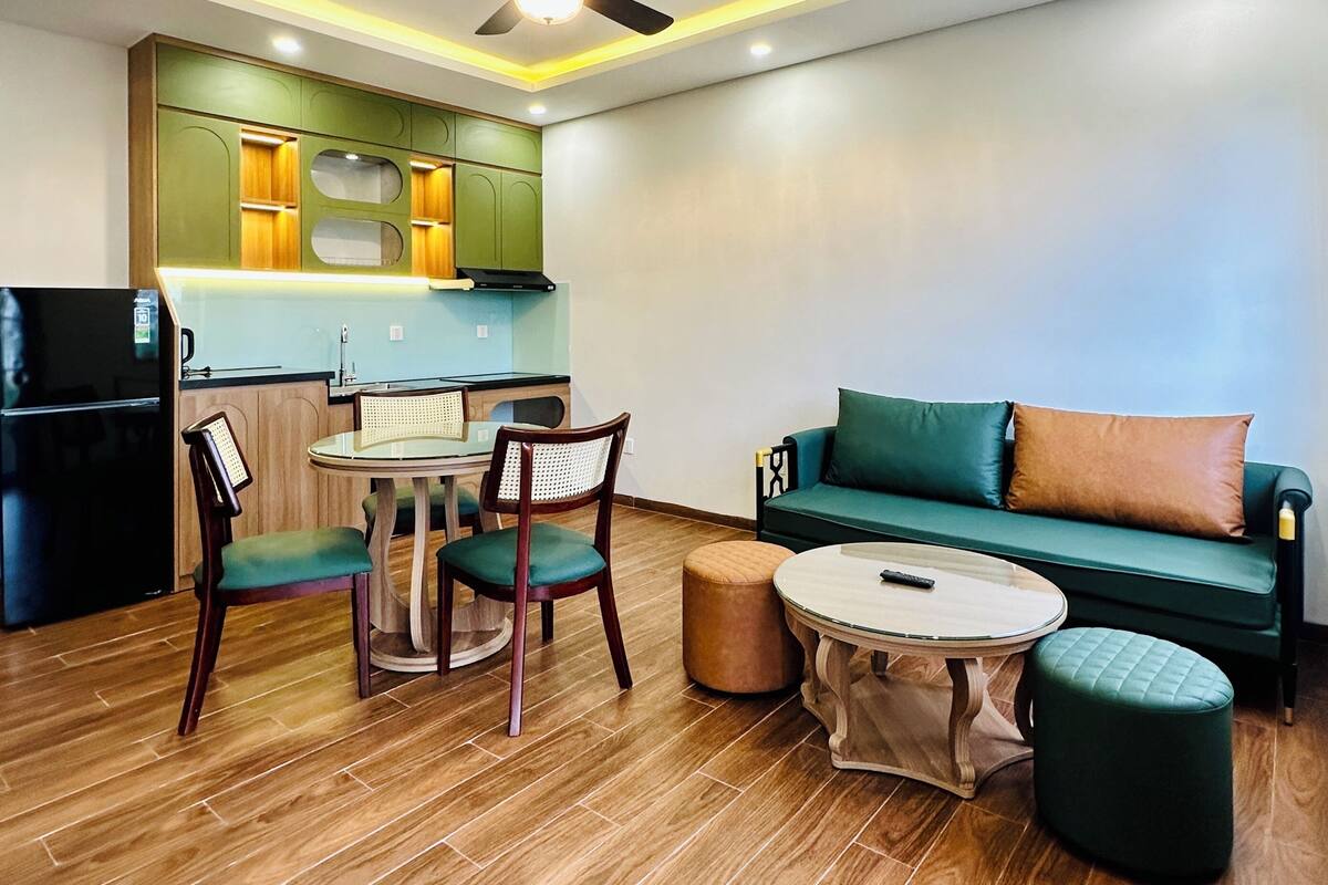 A modern living room with a green sofa, a dining table with chairs, and a ceiling fan.