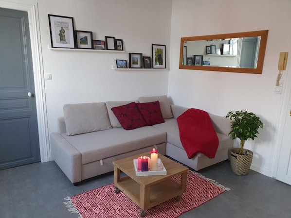 A living room with a sofa, a coffee table with candles, a mirror, and framed pictures on the wall.