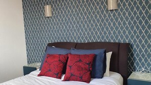Un letto con una testiera decorata, due abat-jour e un comodino blu.
