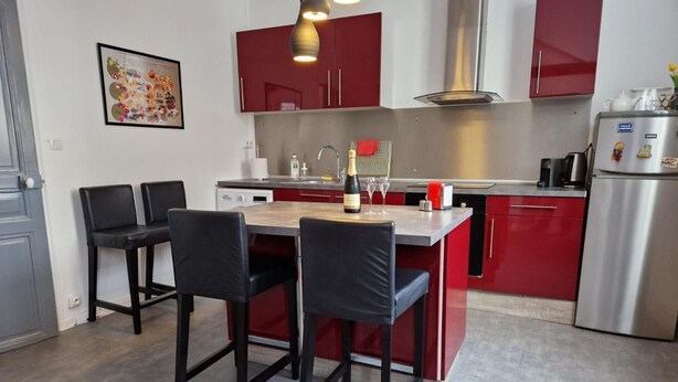 Una cucina moderna con mobili rossi, un frigorifero in acciaio inossidabile, un tavolo da pranzo con sedie e una lampada a sospensione.