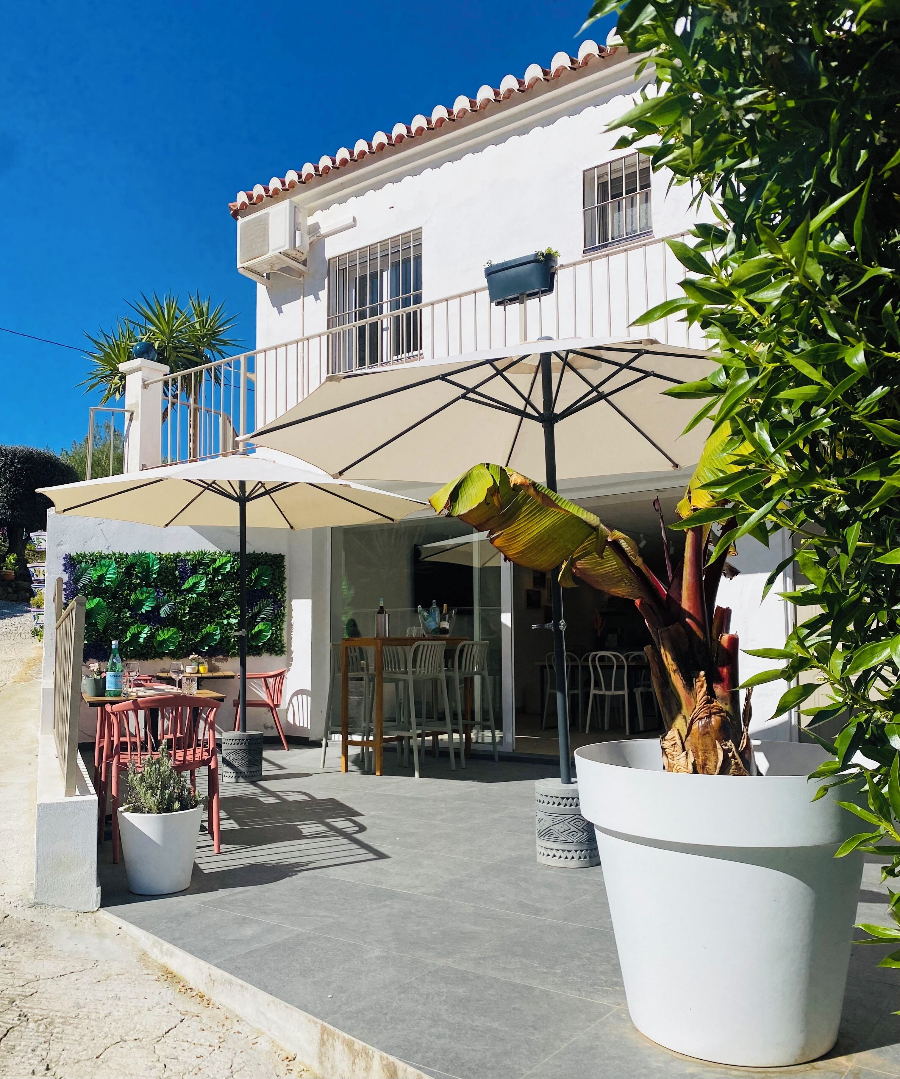 A white building with a balcony, outdoor seating, and potted plants.